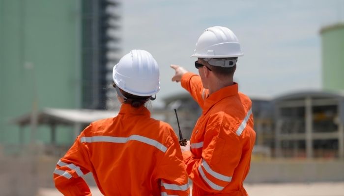 Two construction workers in orange safety gear and helmets stand on-site.