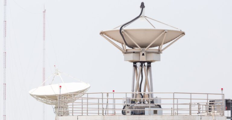 A tall communication tower featuring a large satellite dish at the top